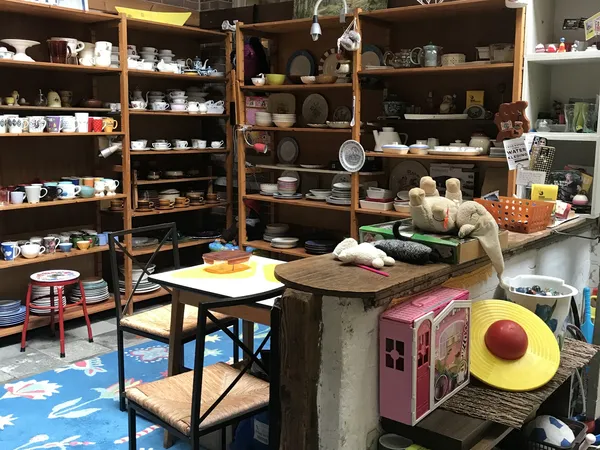 Interieur van kringloopwinkel met houten stellingen vol servies, keramiek en huishoudartikelen, tafel in midden, decorstukken
