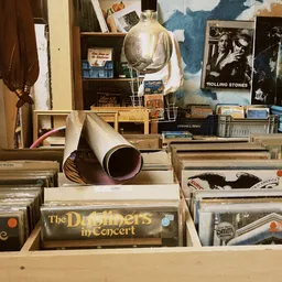 Verzameling LP's en vinyl records in kratten, waaronder 'The Dubliners in Concert' en Rolling Stones poster op de achtergrond