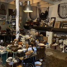 Overzicht van kringloopwinkel met diverse tweedehands spullen, servies, lampen en decoratie op tafels en stellingen
