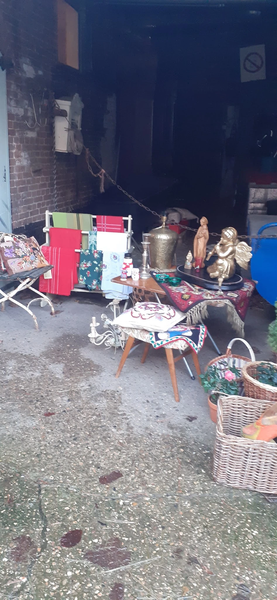 Uiteenlopende tweedehands spullen op en rond een tafel: textiel, decoratieve objecten, beeldjes en huishoudartikelen