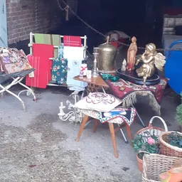 Uiteenlopende tweedehands spullen op en rond een tafel: textiel, decoratieve objecten, beeldjes en huishoudartikelen