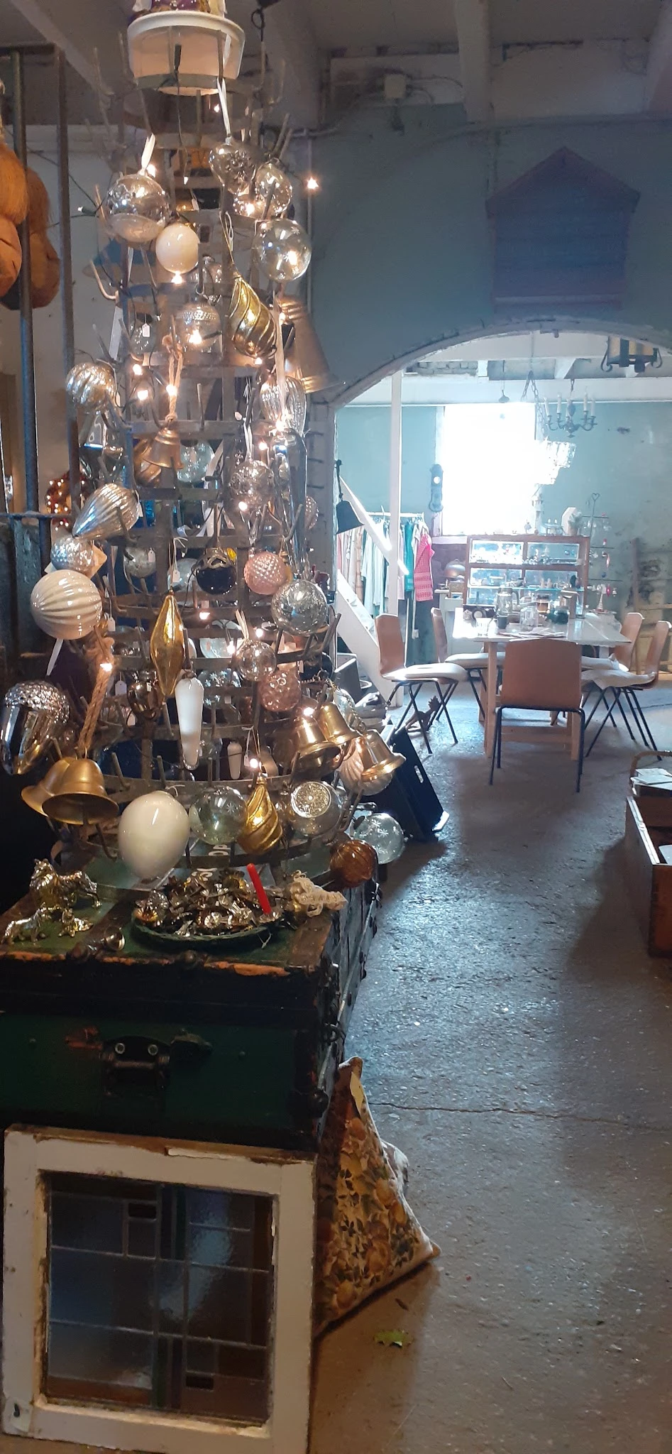Uitgestalde decoratieve items in goud- en zilvertinten, waaronder bollen, lampen en andere huisraad in de kringloopwinkel