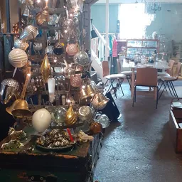 Uitgestalde decoratieve items in goud- en zilvertinten, waaronder bollen, lampen en andere huisraad in de kringloopwinkel