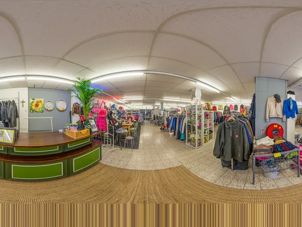 Panoramisch overzicht van kringloopwinkel met kledingrekken, toonbank en horeca-hoekje