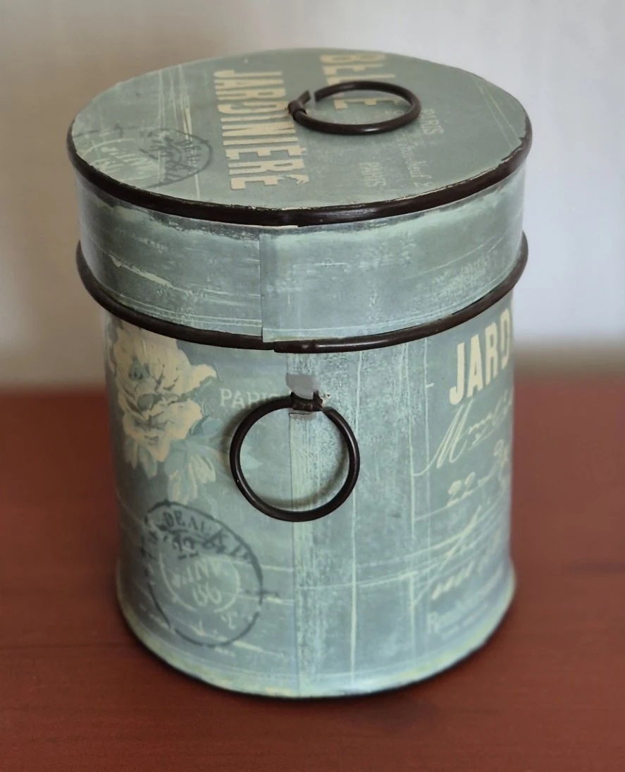 Close-up van een vintage metalen pot of blik met groene patina, zwarte band en ring, mogelijk decoratief of uit een oude keuk