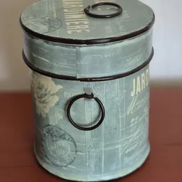 Close-up van een vintage metalen pot of blik met groene patina, zwarte band en ring, mogelijk decoratief of uit een oude keuk