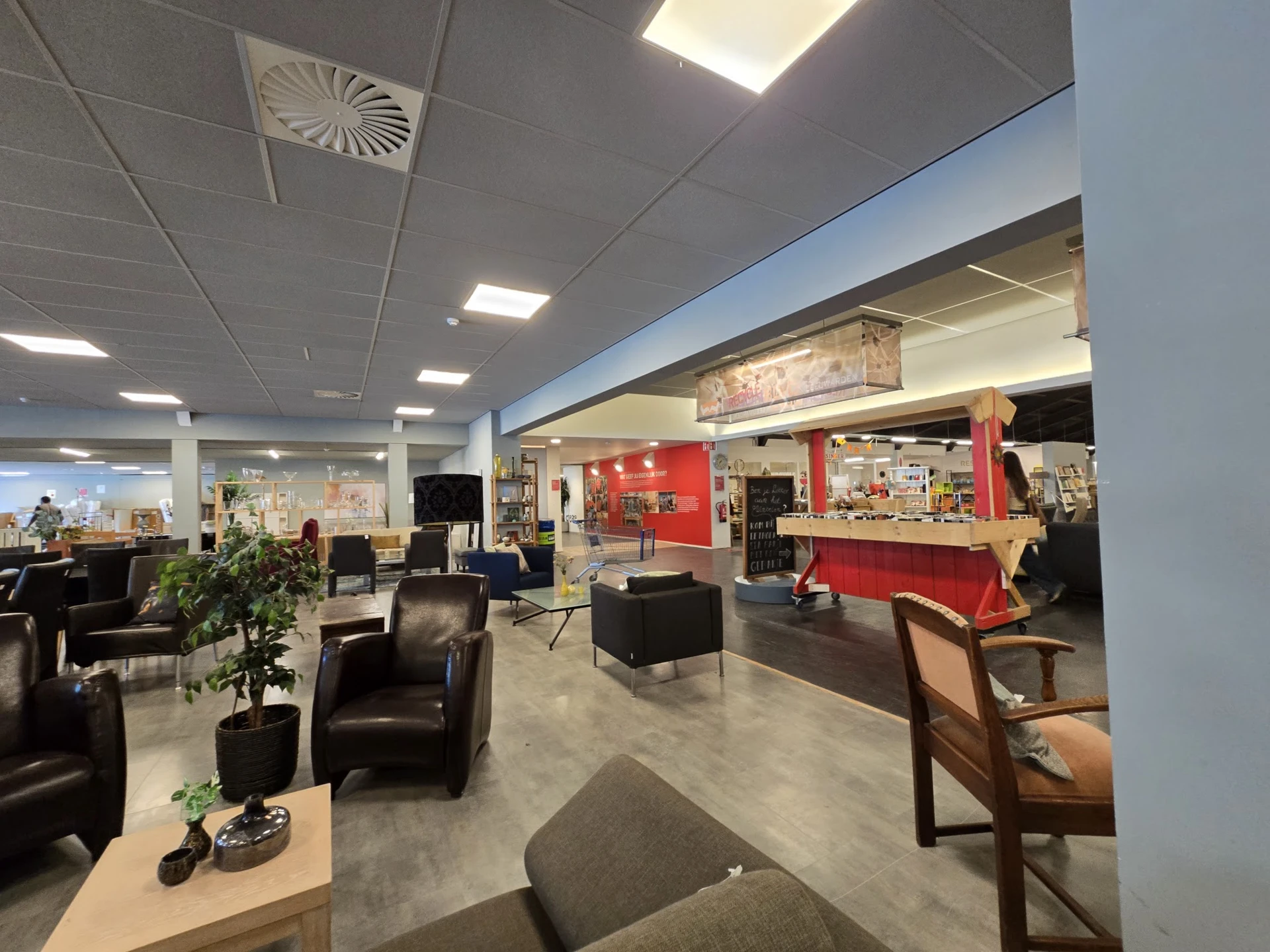 Ruim interieur van kringloopwinkel met zwarte fauteuils, zithoeken, diverse meubels en stellingen met spullen