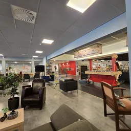 Ruim interieur van kringloopwinkel met zwarte fauteuils, zithoeken, diverse meubels en stellingen met spullen