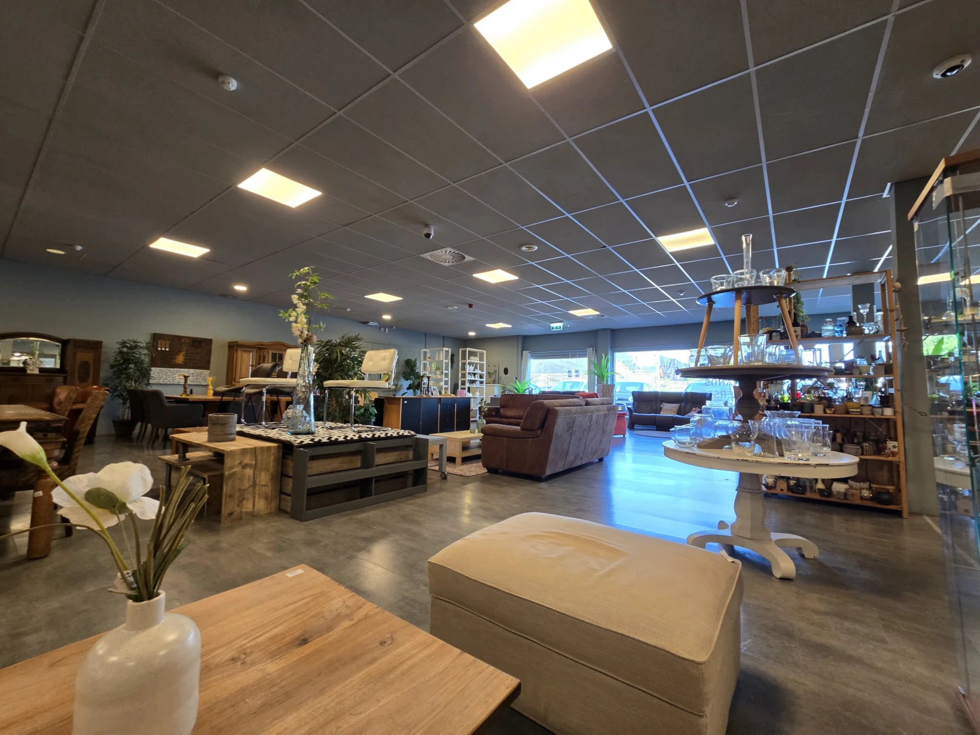 Ruim winkelbinnenland met grijze betonvloer, diverse meubels en huishoudartikelen uitgestald, plafond met LED-verlichting en 