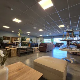 Ruim winkelbinnenland met grijze betonvloer, diverse meubels en huishoudartikelen uitgestald, plafond met LED-verlichting en 