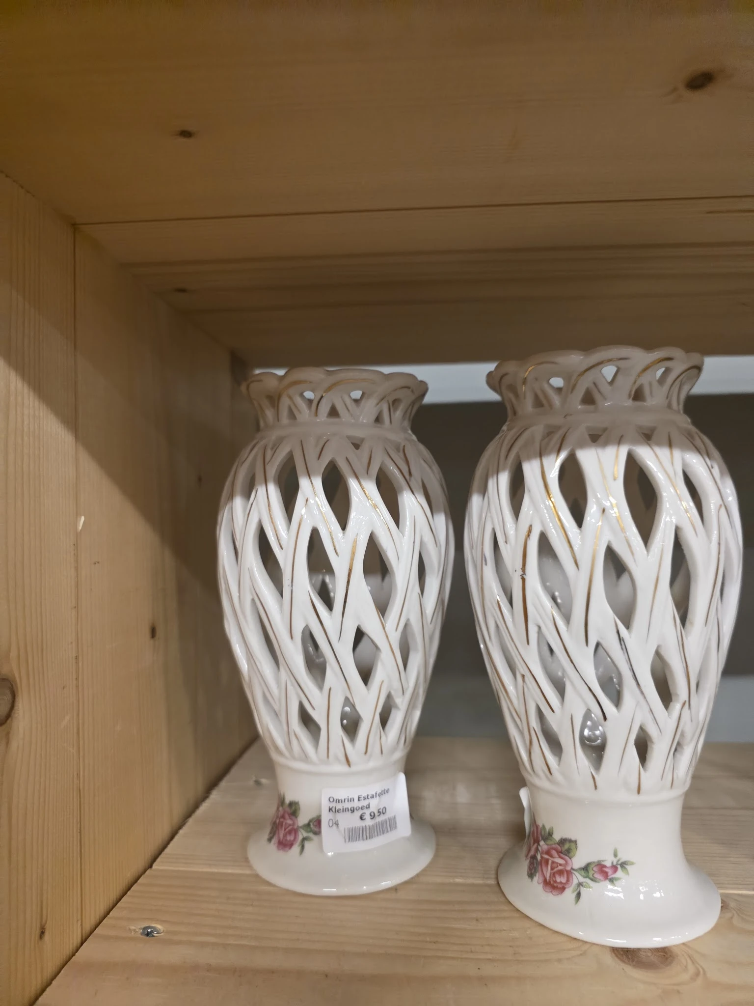 Twee witte opengewerkte decoratieve vazen met patroon, op een plank in de winkel
