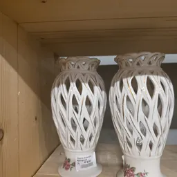 Twee witte opengewerkte decoratieve vazen met patroon, op een plank in de winkel