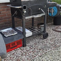 Tweedehandsartielen op een karretje buiten: serviesgoed, stapels papier en een rode plastic krat