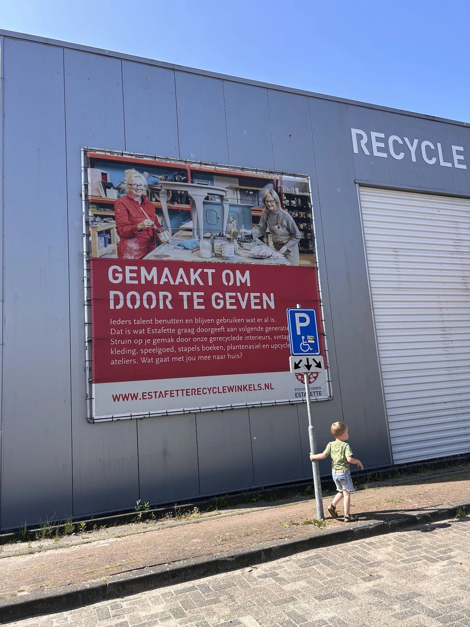 Groot reclamebord aan gevel met afbeelding en Nederlandse tekst, gedeeltelijk zichtbare winkelwand