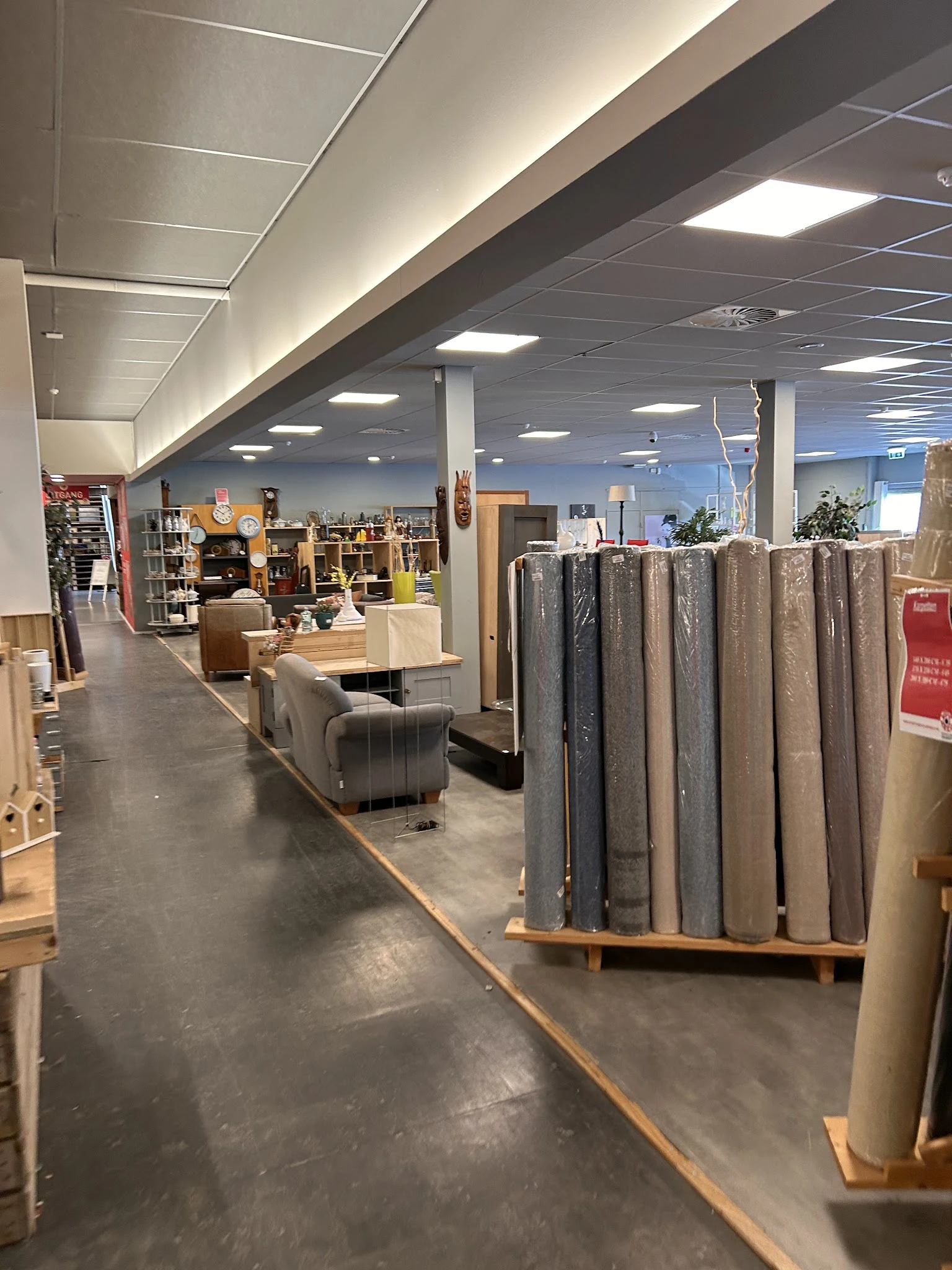Winkelvloer met uitgestalde meubels, stellingen met artikelen en opgerolde tapijten/vloerbedekking op pallets