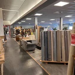 Winkelvloer met uitgestalde meubels, stellingen met artikelen en opgerolde tapijten/vloerbedekking op pallets