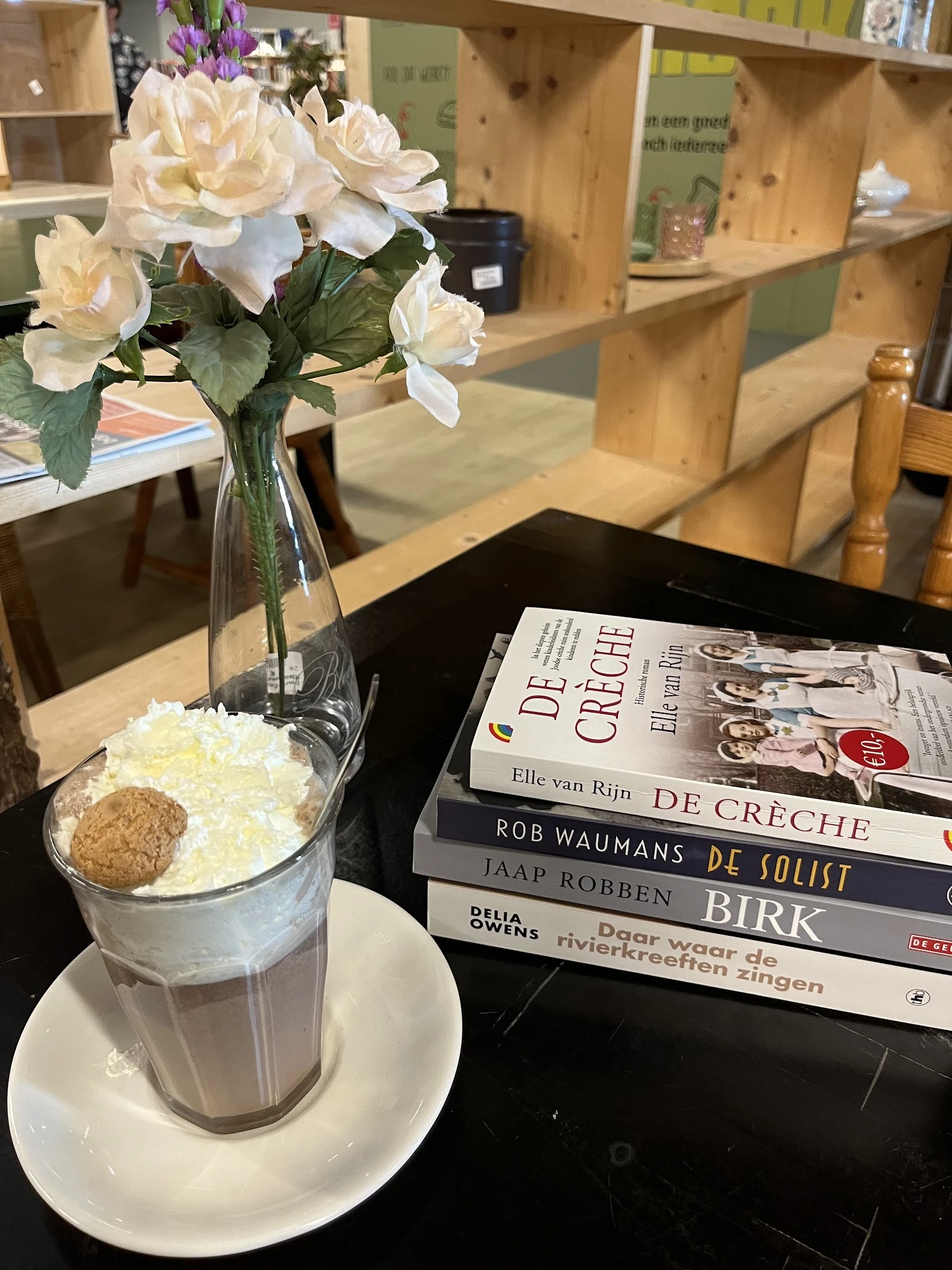 Tafel met bloemen in vaas, stapel boeken en glas met ijs in een winkelinterieur