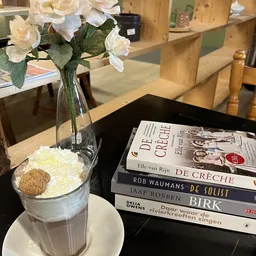 Tafel met bloemen in vaas, stapel boeken en glas met ijs in een winkelinterieur