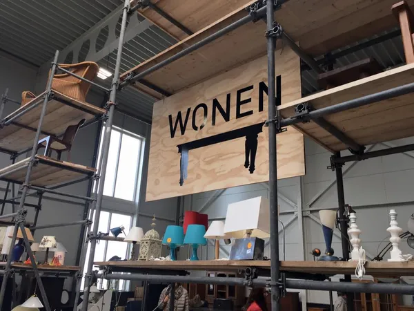 Winkelinterieur met steigers, houten borden met 'WOMEN' opschrift en uiteenlopend huishoudelijk aanbod
