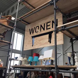 Magazijnruimte met stellingen, bord met 'WOMEN' opschrift en diverse spullen op planken