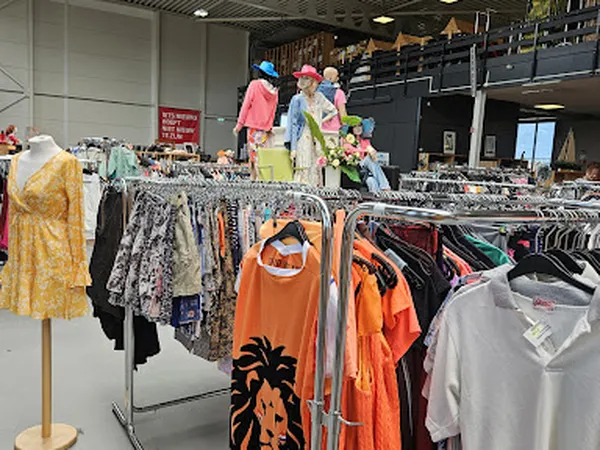 Rekken met tweedehands kleding in diverse kleuren en stijlen, waaronder oranje shirts en jurken in verschillende maten