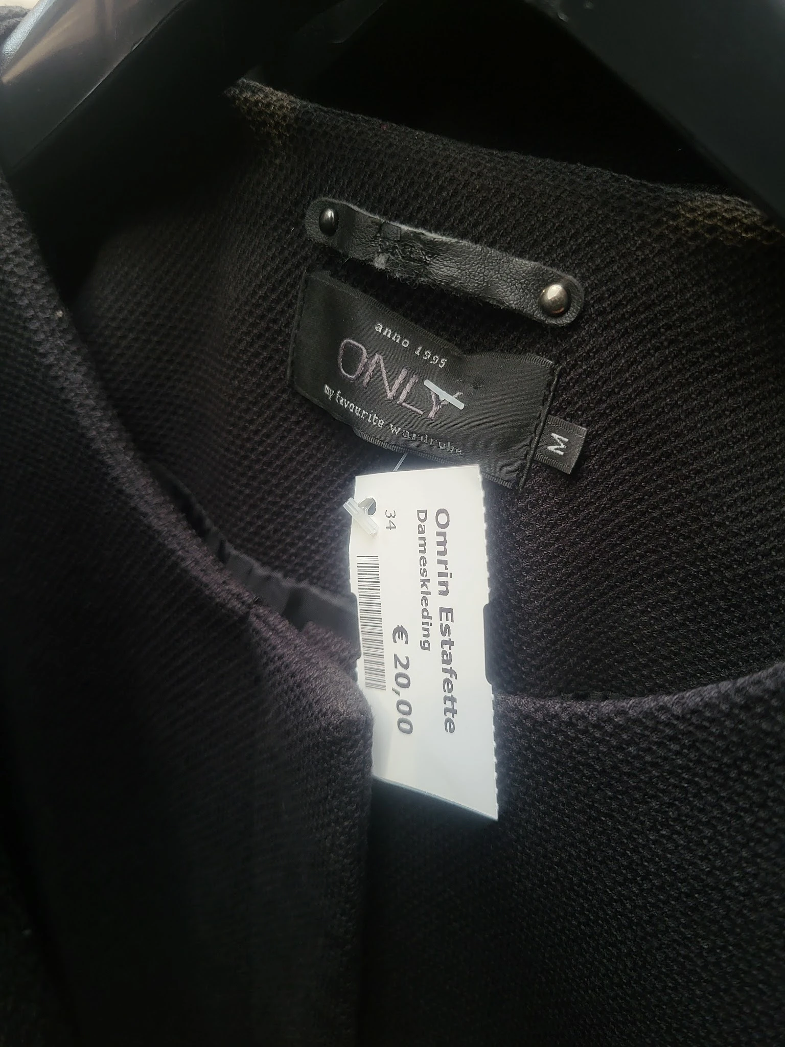 Zwart kledingstuk met prijskaartje van €20,00 en merklabel 'Estafette'