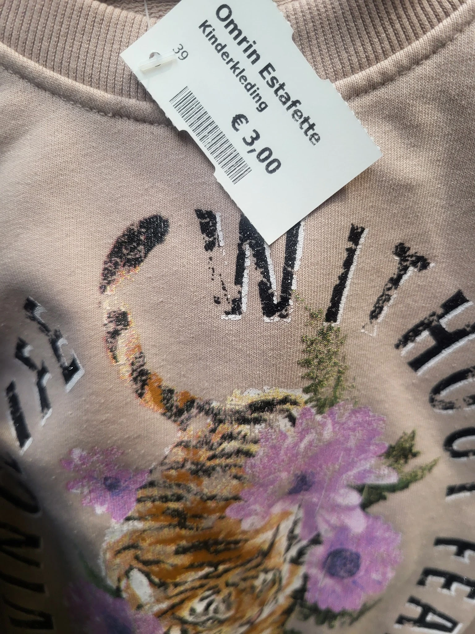 Close-up van een beige trui met grafisch print van bloemen en tekst