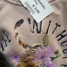 Close-up van een beige trui met grafisch print van bloemen en tekst