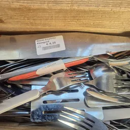 Verzameling gebruikte bestek en servies op metalen oppervlak met prijskaartje