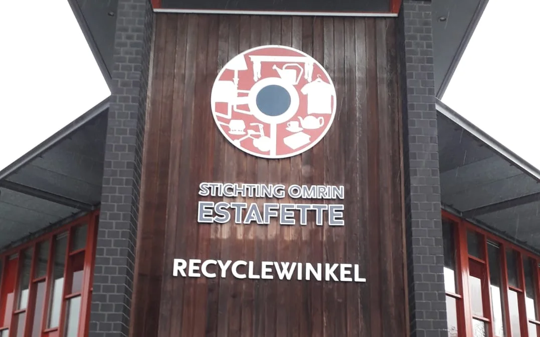 Voorgevel van kringloopwinkel met logo en tekst 'Stichting Omrin Estafette Recyclewinkel' op houten deur