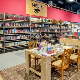 Mediaafdeling in kringloopwinkel met boekenrekken tegen roze wand en houten tafel met stoelen waarop boeken uitgestald