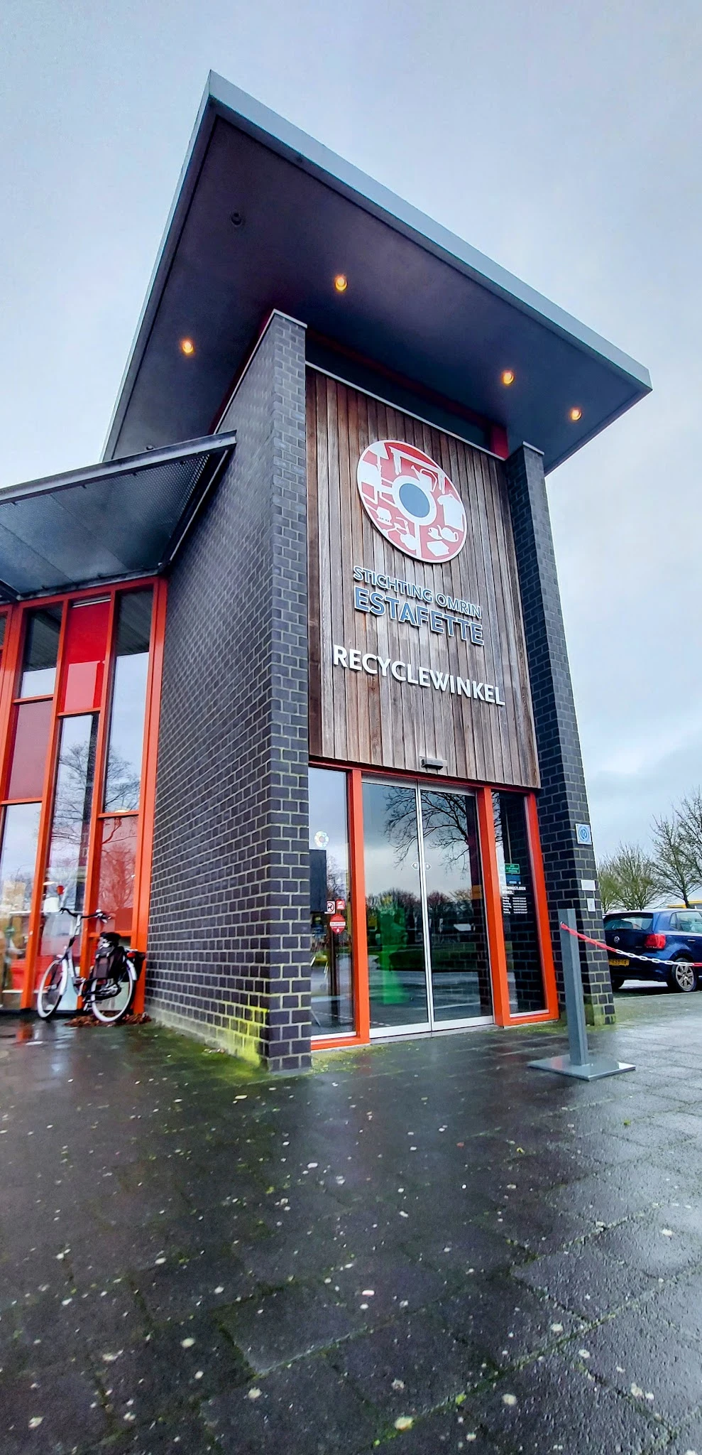 Gevel van kringloopwinkel Estafette Recyclewinkel met rode deuren en naam op gevelsteen