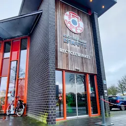 Gevel van kringloopwinkel Estafette Recyclewinkel met rode deuren en naam op gevelsteen