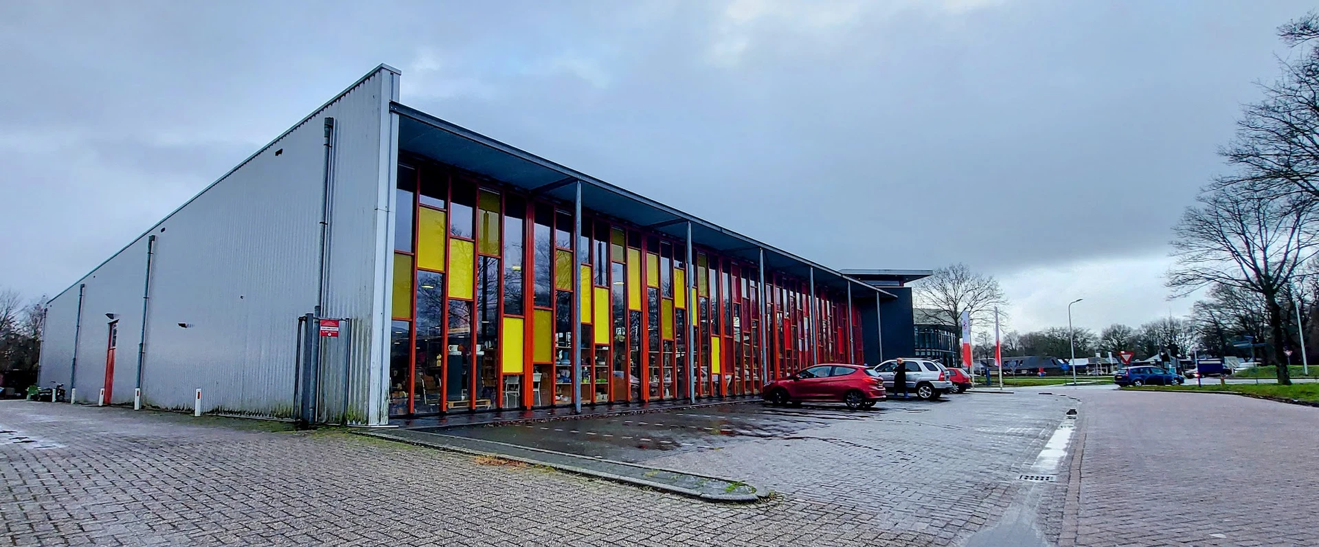 Moderne gevel van recyclewinkel met gele en rode deuren en grote raampartijen, parkeerplaats met auto's ervoor