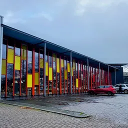 Moderne gevel van recyclewinkel met gele en rode deuren en grote raampartijen, parkeerplaats met auto's ervoor