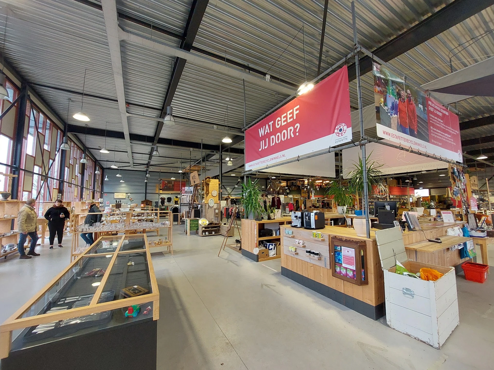 Ruim magazijnachtig interieur van een kringloopwinkel met diverse stellingen, displays en artikelen