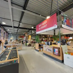 Ruim magazijnachtig interieur van een kringloopwinkel met diverse stellingen, displays en artikelen