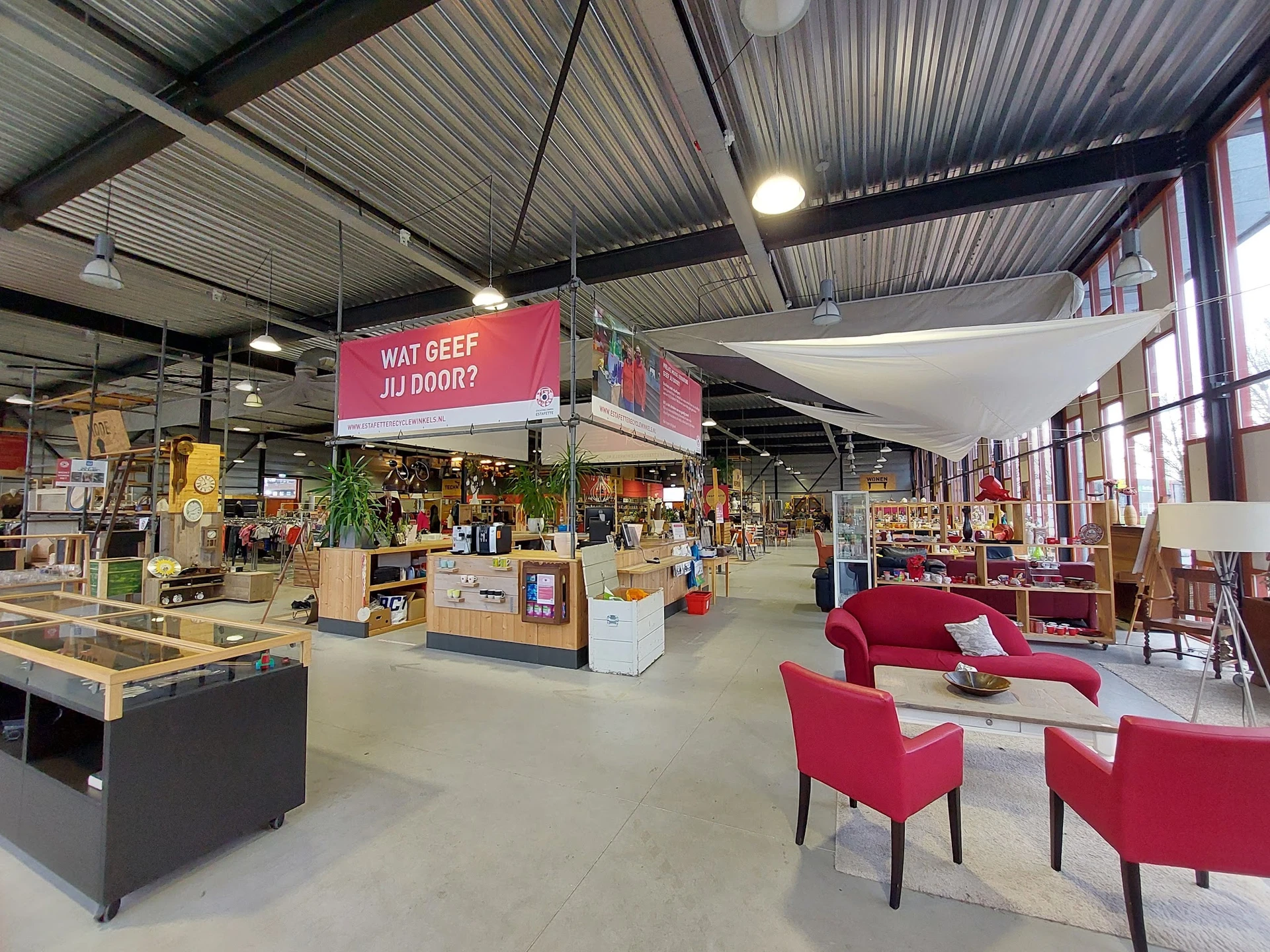 Ruime winkelruimte met houten werkbanken, stellingen met spullen, rode designmeubels en roze winkellogo aan het plafond