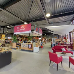 Ruime winkelruimte met houten werkbanken, stellingen met spullen, rode designmeubels en roze winkellogo aan het plafond