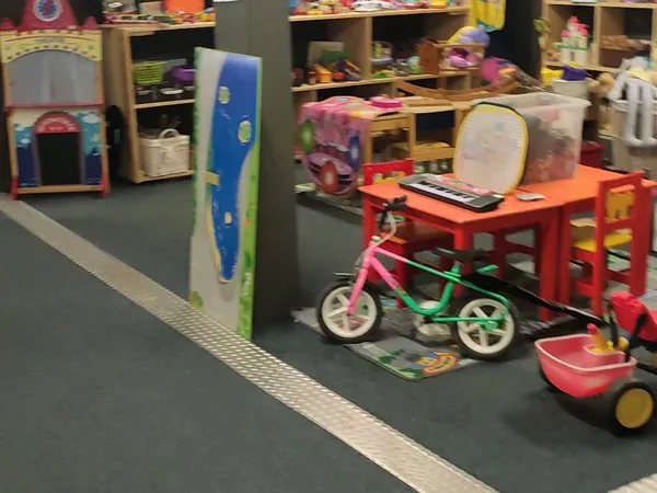 Speelgoedafdeling met kinderfietsjes, rode tafels, speelgoed en opbergrekken in kringloopwinkel