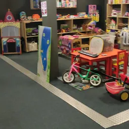 Speelgoedafdeling met kinderfietsjes, rode tafels, speelgoed en opbergrekken in kringloopwinkel