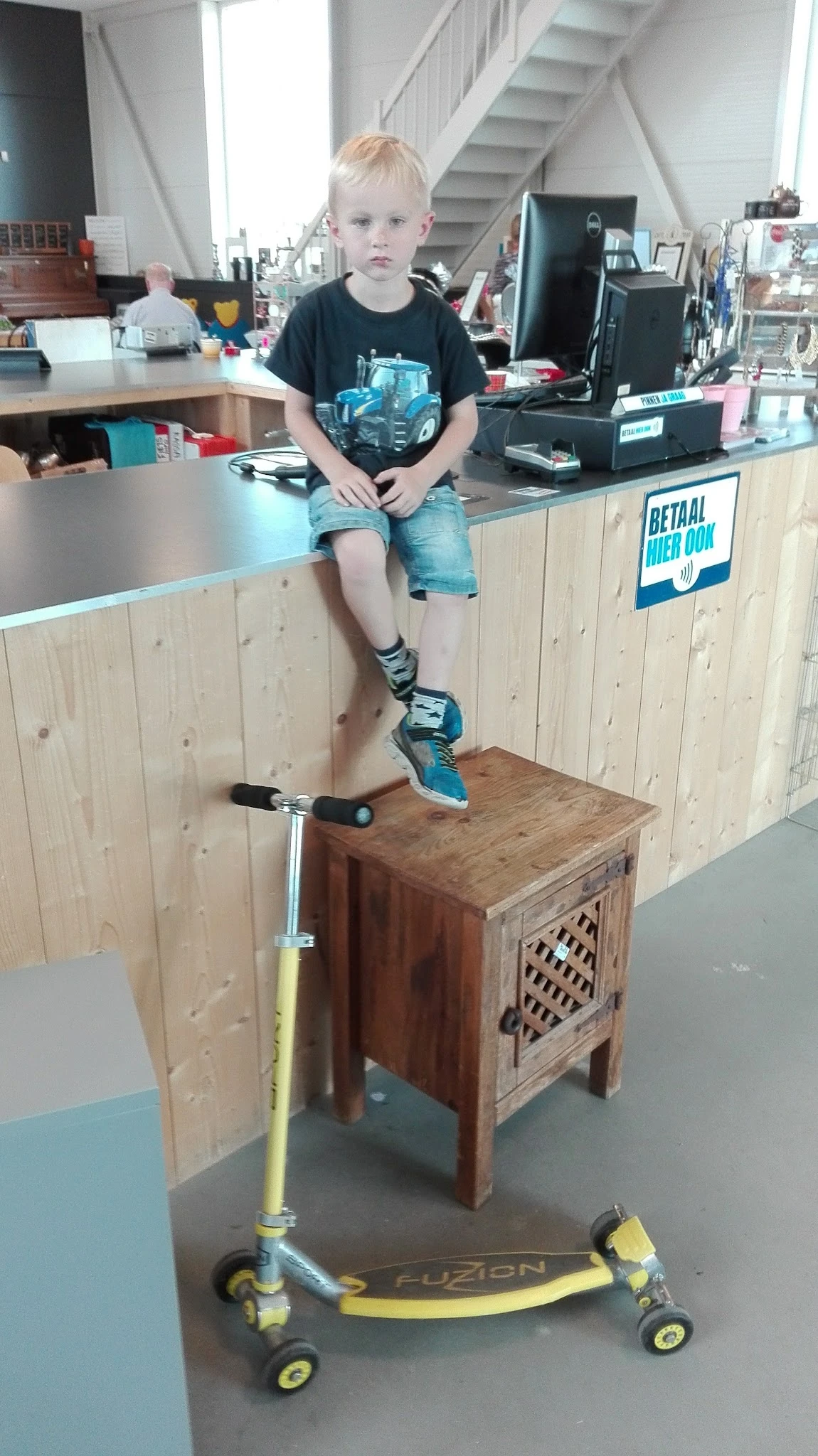 Persoon zittend op houten meubel met een step, draagt blauwe schoenen en sokken