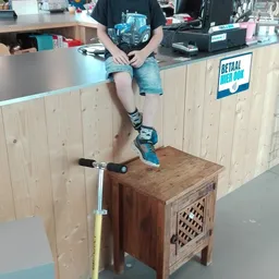Persoon zittend op houten meubel met een step, draagt blauwe schoenen en sokken