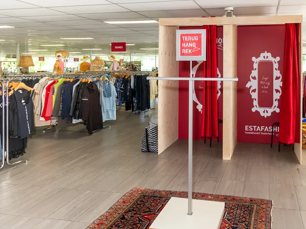 Winkelvloer met kledingrekken en een rode paskamer met decoratieve rand en ESTAFASHI-logo