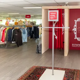 Winkelvloer met kledingrekken links en rode winkelstand rechts met decoratie