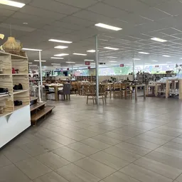 Ruime winkelvloer met houten tafels en stoelen, stellingen met spullen, goed verlicht interieur