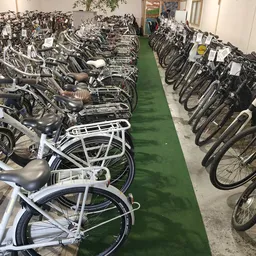 Rijen tweedehandsfietsen in verschillende kleuren opgesteld in een opslagruimte met groene vloer.