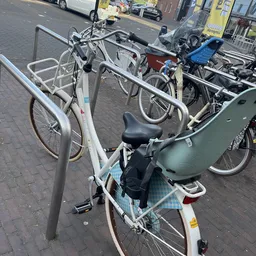 Verschillende tweedehandsfietsenen fietsen in standaards op een parkeerplaats.