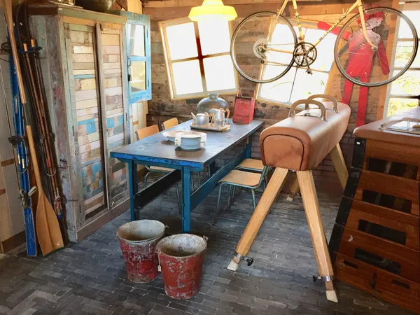 Winkelbinnenruimte met blauwe tafel, stoelen, vintage fiets aan muur, oude deuren en diverse tweedehandsartikelen