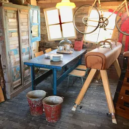 Winkelbinnenruimte met blauwe tafel, stoelen, vintage fiets aan muur, oude deuren en diverse tweedehandsartikelen